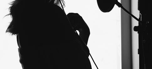 A dramatic silhouette of a woman singing into a microphone in a recording studio.