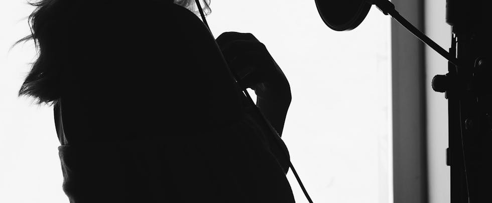 A dramatic silhouette of a woman singing into a microphone in a recording studio.