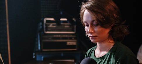 A focused woman manages an audio mixer in a recording studio setting.