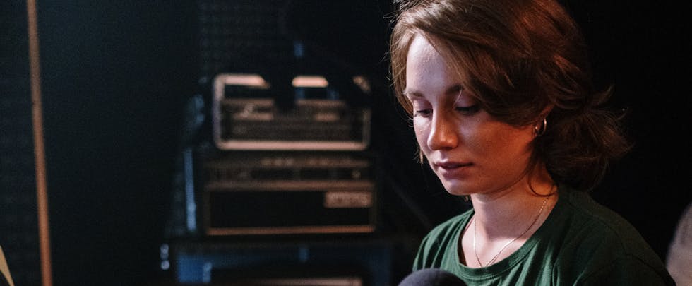 A focused woman manages an audio mixer in a recording studio setting.