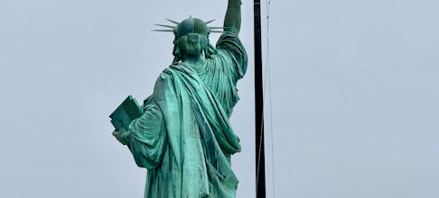 Back view of the Statue of Liberty with the American flag waving in the background.
