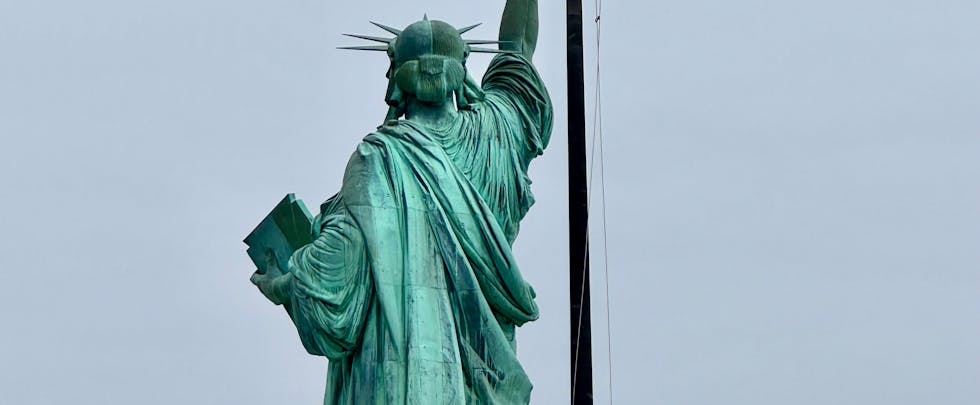 Back view of the Statue of Liberty with the American flag waving in the background.