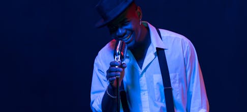 Black male jazz singer smiling while performing with vintage microphone and blue lighting.