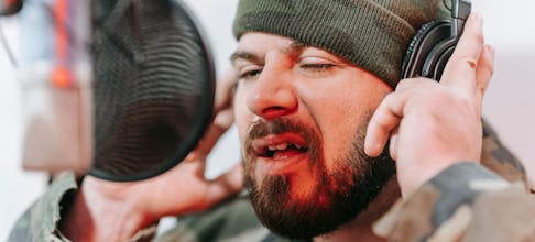 Close-up of a musician recording vocals in a studio, wearing headphones and camouflage.