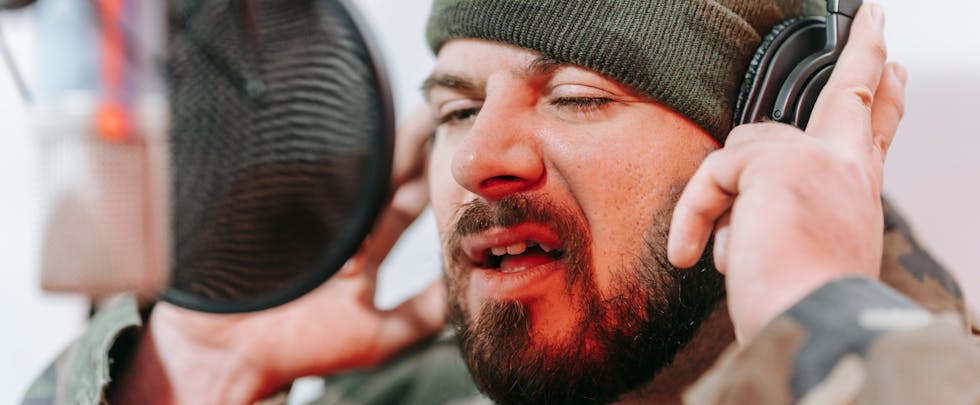 Close-up of a musician recording vocals in a studio, wearing headphones and camouflage.