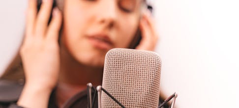 Close-up of a woman singing into a studio microphone, eyes closed, expressing emotion.