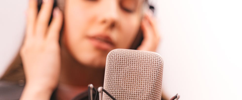 Close-up of a woman singing into a studio microphone, eyes closed, expressing emotion.