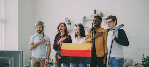 Excited friends celebrate sports with flag and anthem indoors.