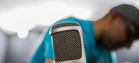Focused shot of a condenser microphone in a recording studio with a person in the background.