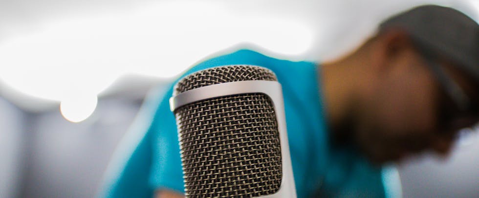Focused shot of a condenser microphone in a recording studio with a person in the background.