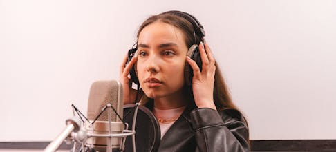 Woman in a leather jacket recording vocals in a professional studio.