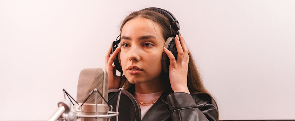 Woman in a leather jacket recording vocals in a professional studio.