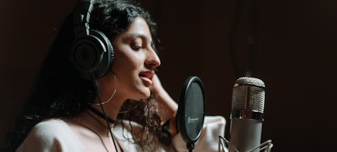 Woman in a music studio singing into a microphone, wearing headphones.