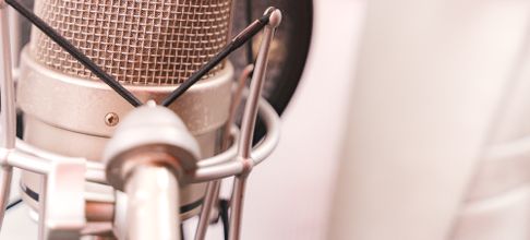 Woman recording music with a condenser microphone in a studio setting.