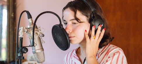 Young woman recording music in a studio with headphones and a microphone pop filter.