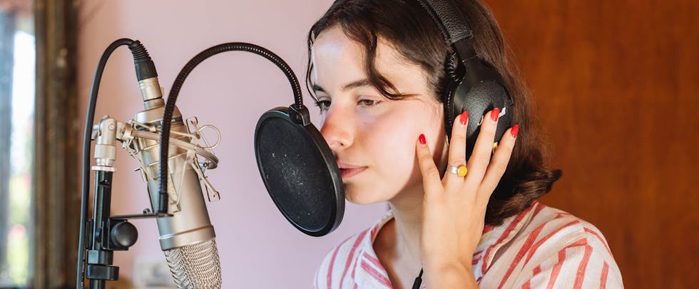 Young woman recording music in a studio with headphones and a microphone pop filter.